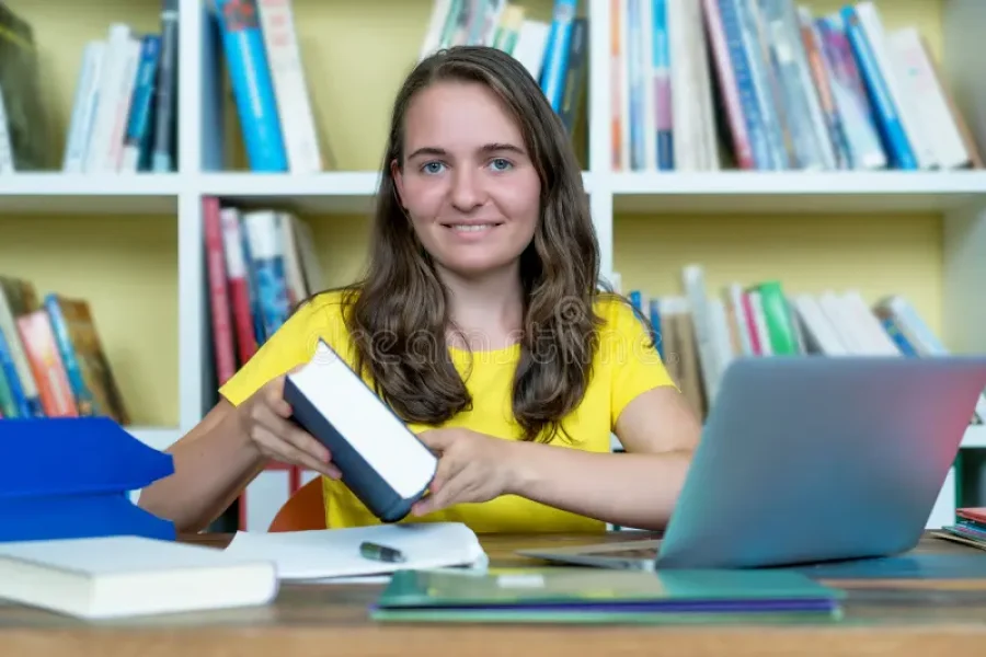 riendo-estudiante-alemana-aprendiendo-libros-y-computadoras-en-el-escritorio-libro-computadora-casa-194271797